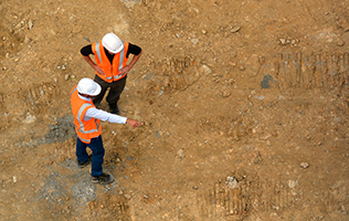 Two construction workers, viewed from above, standing on ground that has been bulldozed.