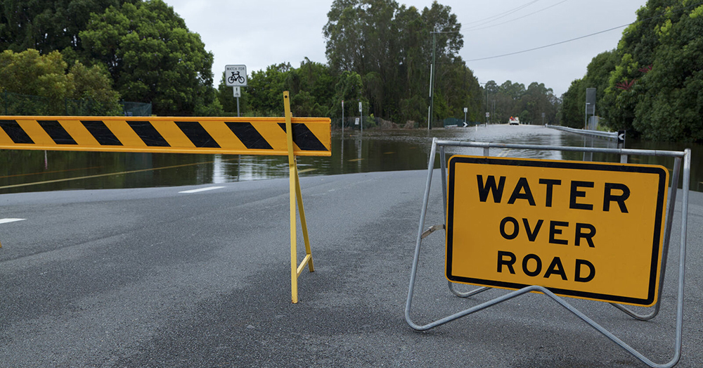 A flooded, closed off road with a sign that reads Water Over Road.
