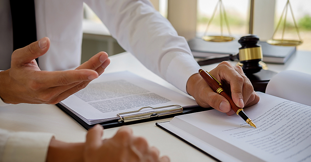 Legal counsel presents to the client a signed contract with gavel and legal law or legal having team meeting at law firm in background.