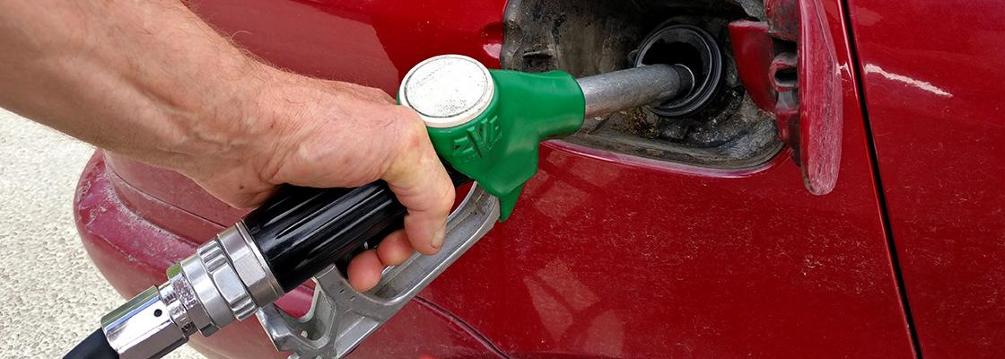 An outstretched arm holding a fuel hose while filling a car with fuel at a service station petrol bowser..
