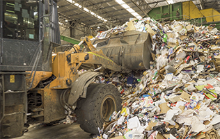 A loader scoops up waste paper and cardboard in a warehouse