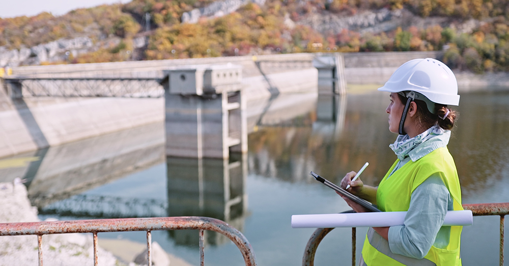A woman in high viz vest and hardhat on a dam wall taking notes.