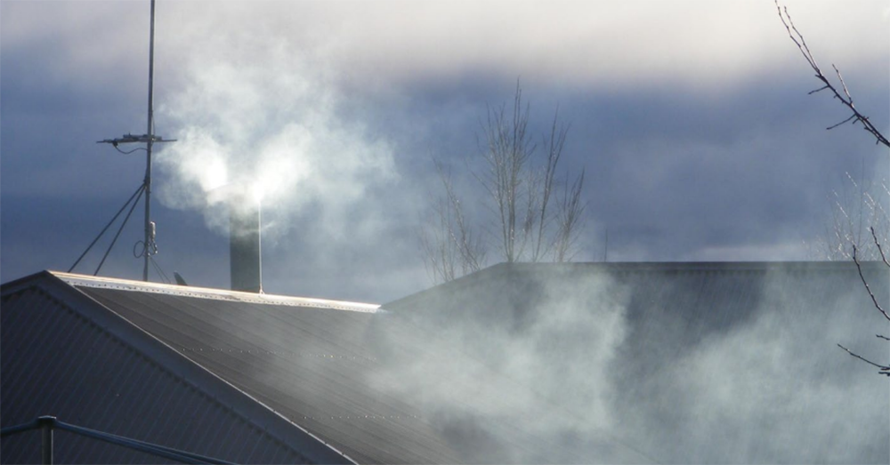 Smoke coming out of a chimney in a suburban home.