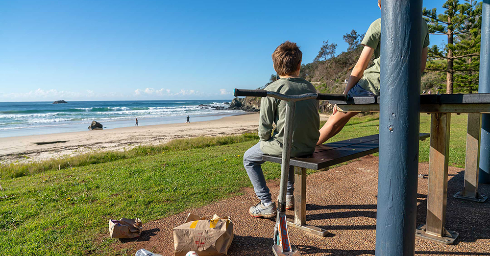 Two kids at a beach who have thrown their Maccas rubbish on the the ground.