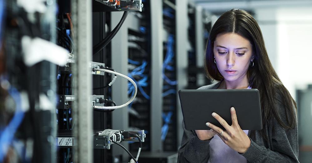 A women with tablet checks a bank of servers.