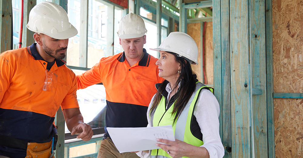Three people in discussion on a work site in high viz and PPE .