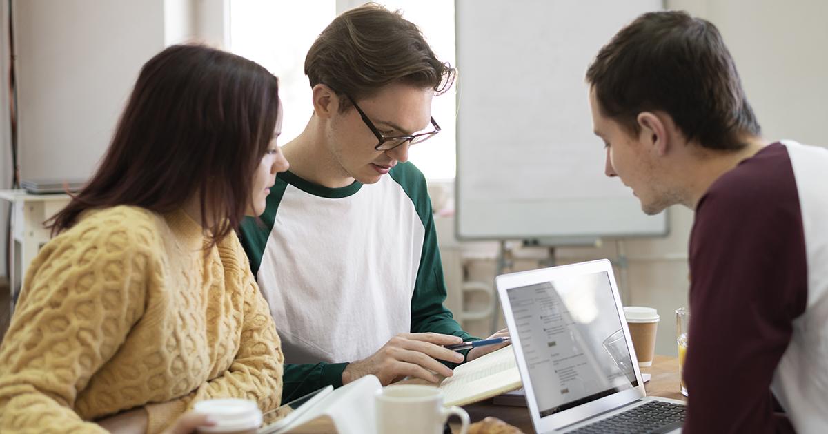 Team members working together at a table, discussing notes and reviewing content on a laptop.