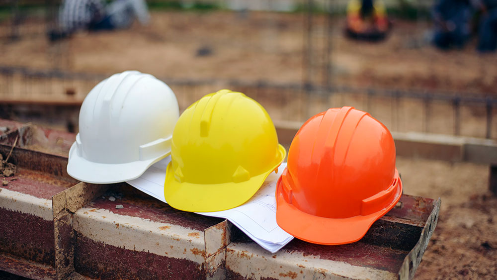 Three hard hats (white, yellow, red) sitting on a pile of bricks at at construction site.