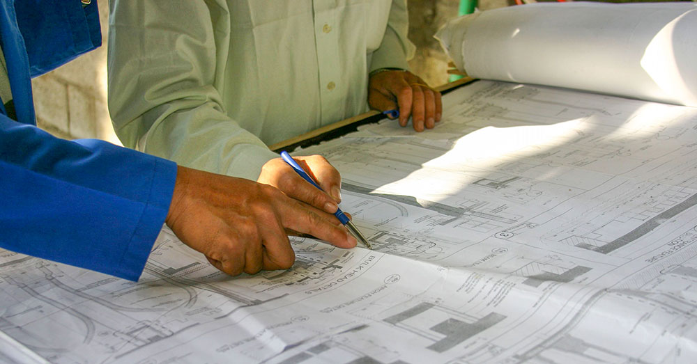 A couple's hand seen pointing at a set of building plans/drawings. 