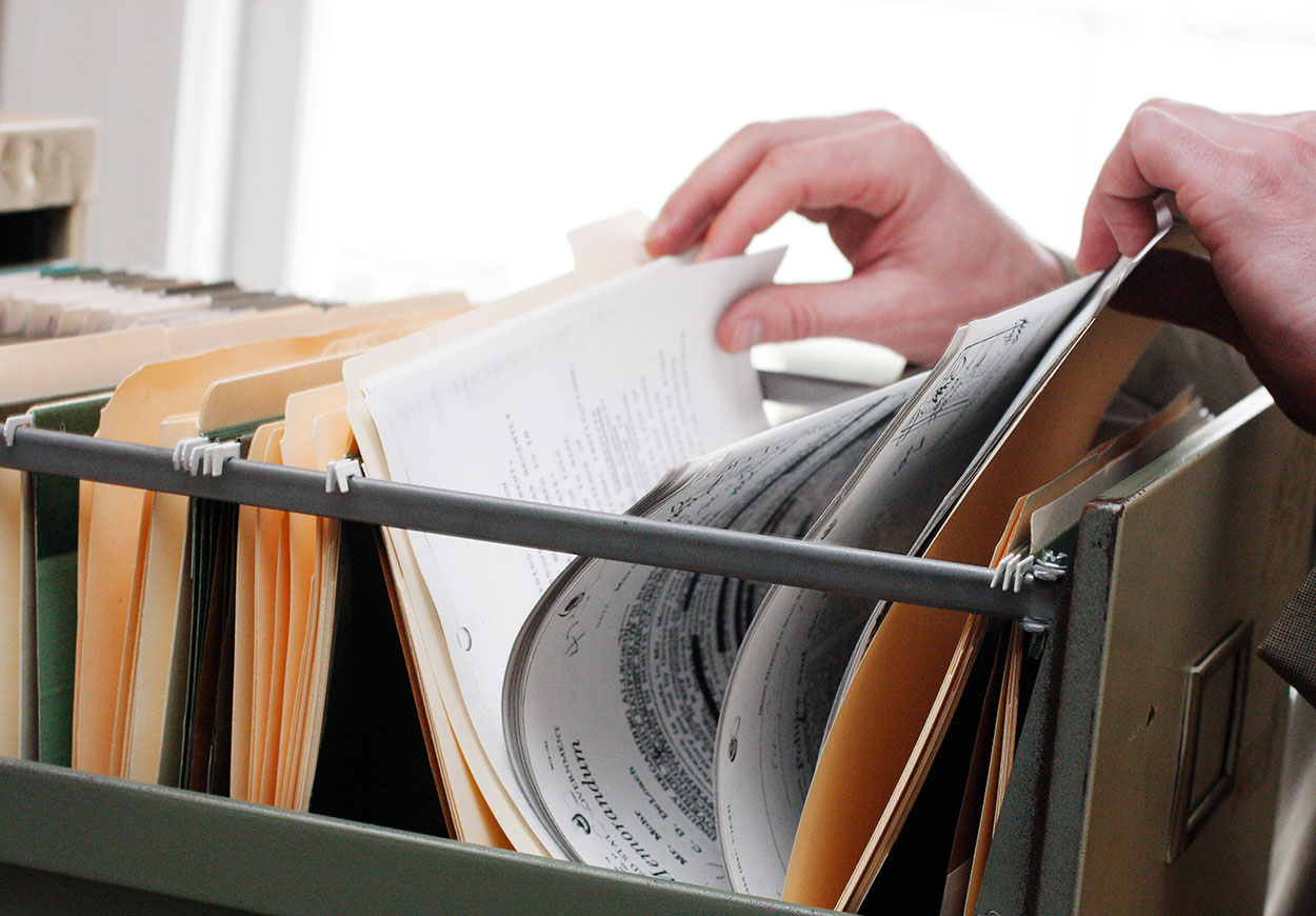 A person thumbing through a file in an open filing cabinet drawer.