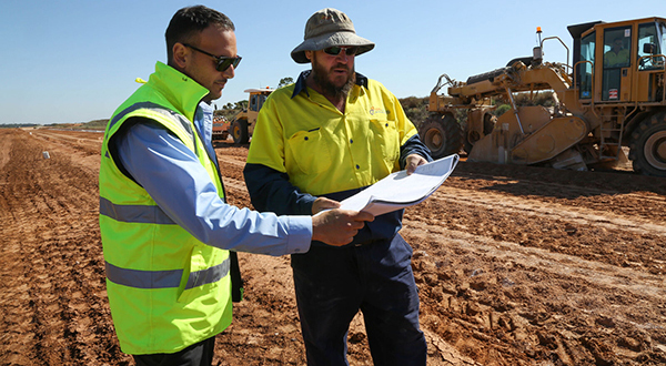 Roadworks crew members reviewing a document on a road being resurfaced.