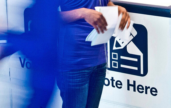 A woman (shown from waist down) leaves a voting booth to cast her vote.