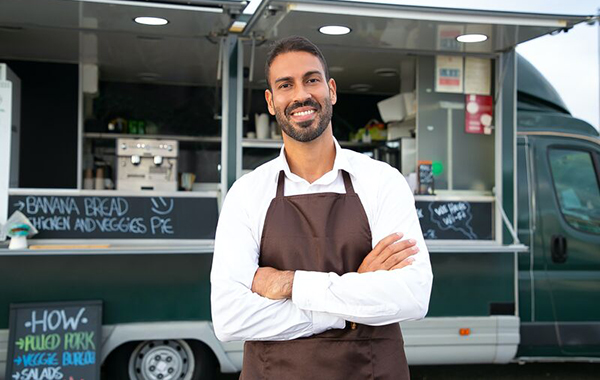 Small business owner stand smiling, arms crossed, in front of his food van.