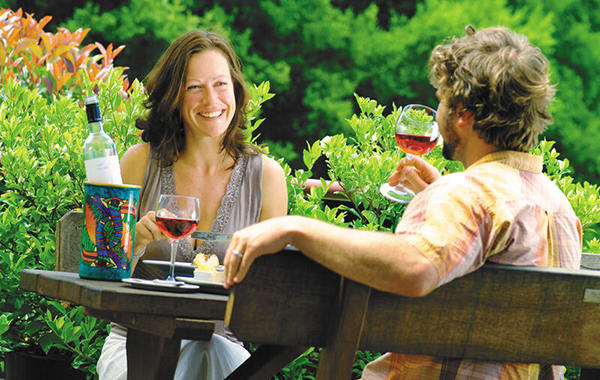 A couple holidaying drink wine at a vineyard.